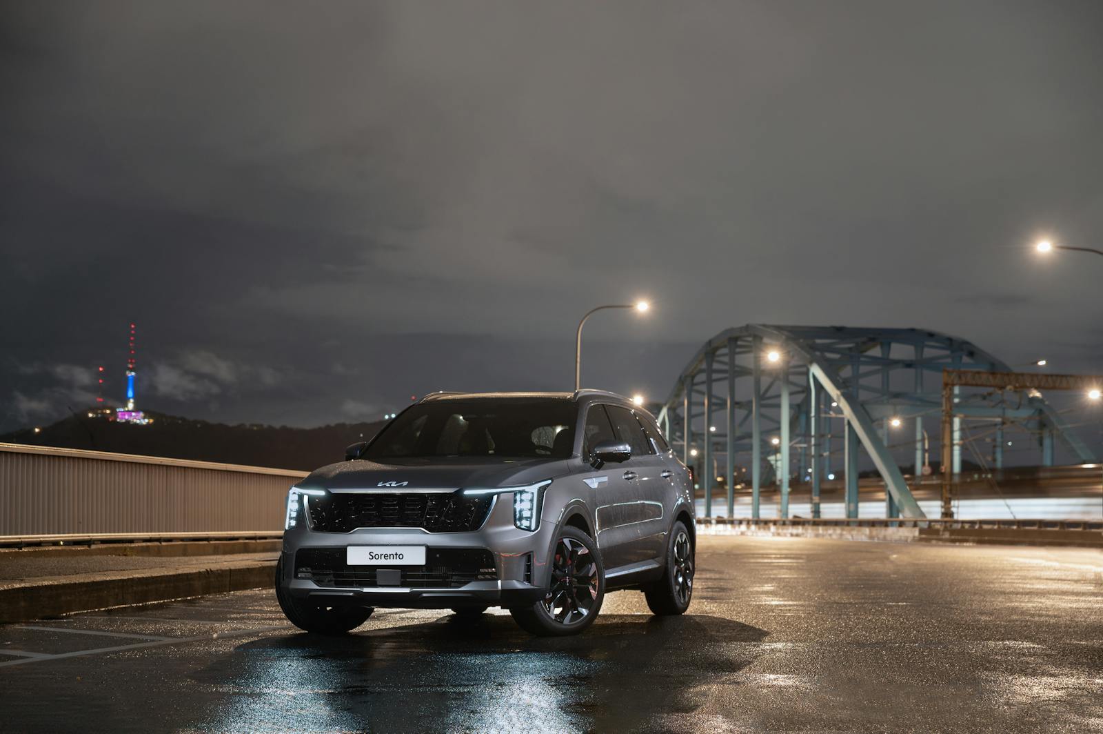 A sleek SUV parked by a lit bridge at night under cloudy skies, showcasing urban elegance.