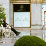 A man holding a bouquet sits on a bench outside shops in Baku, Azerbaijan.