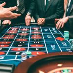 Group of people playing roulette, placing bets in a casino setting.